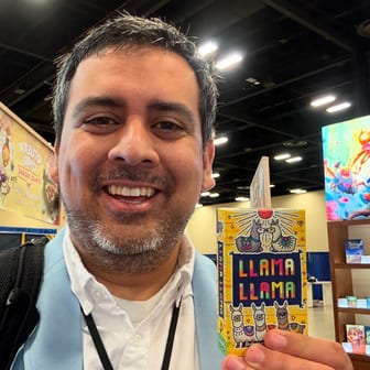 David, the rep who built RepLlama, grinning on a trade-show floor and holding up a Llama Llama card game